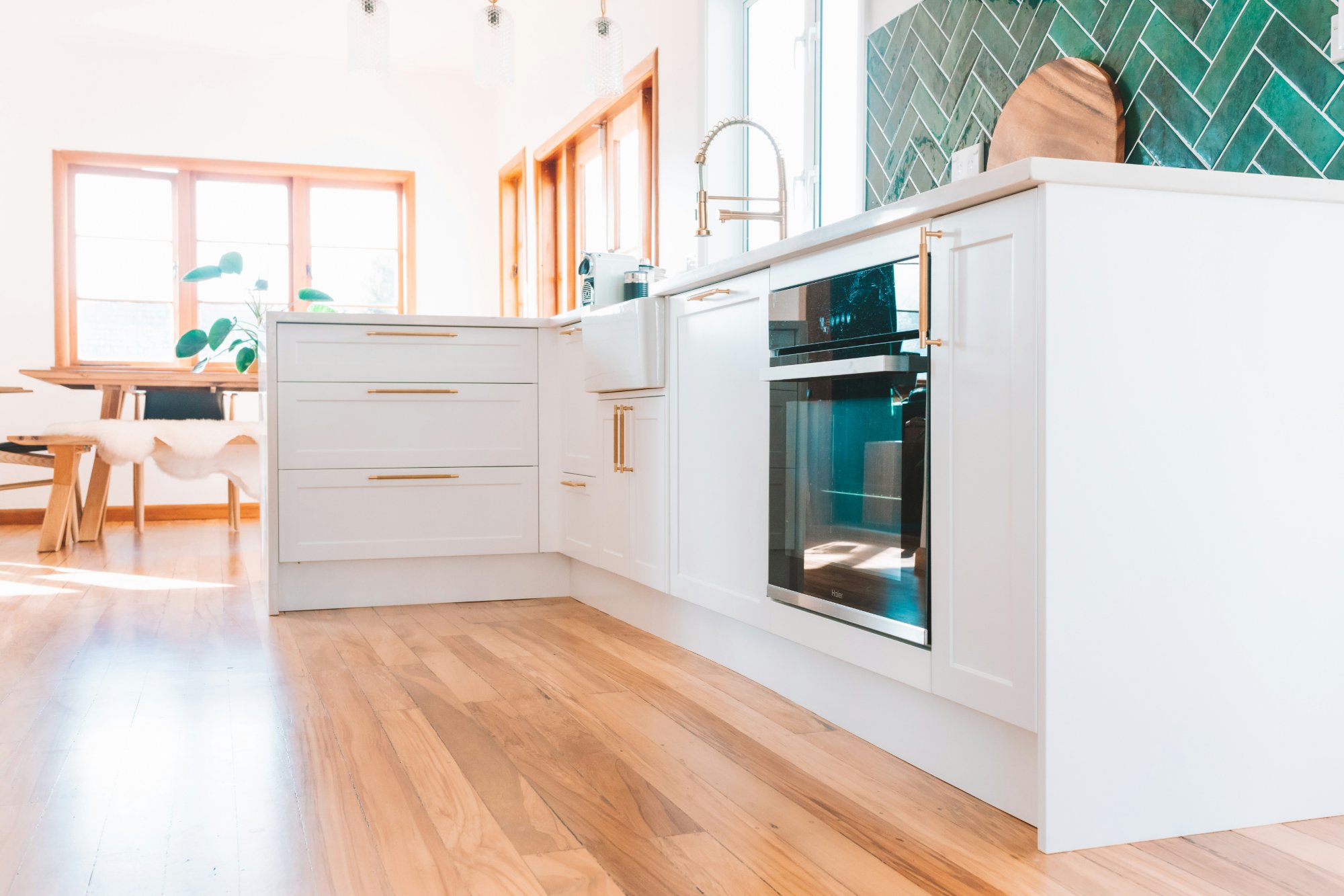 Wide view of white kitchen with timber floors and open plan dining