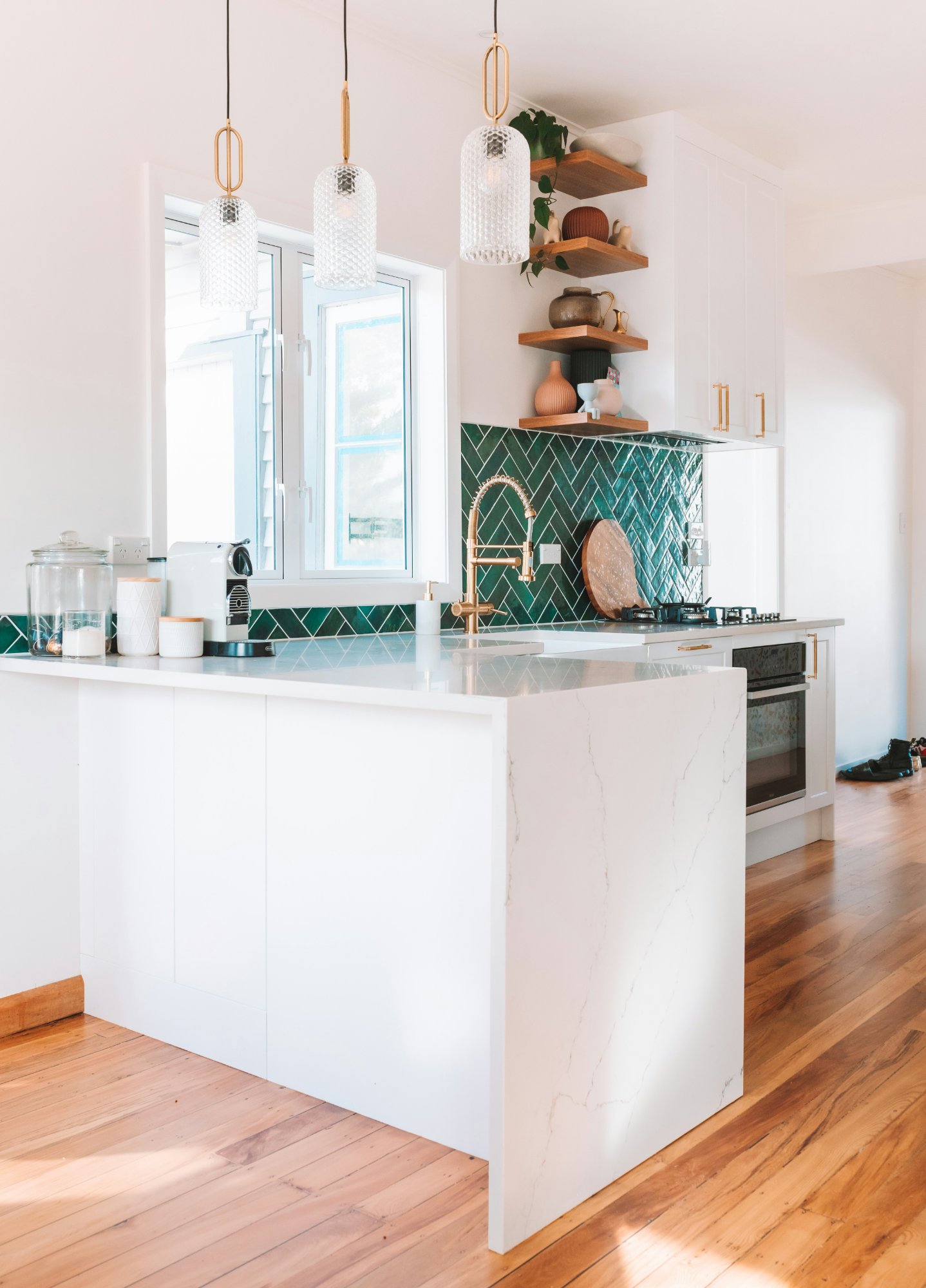 Kitchen island with white cabinetry, marble benchtop and green herringbone tile splashback